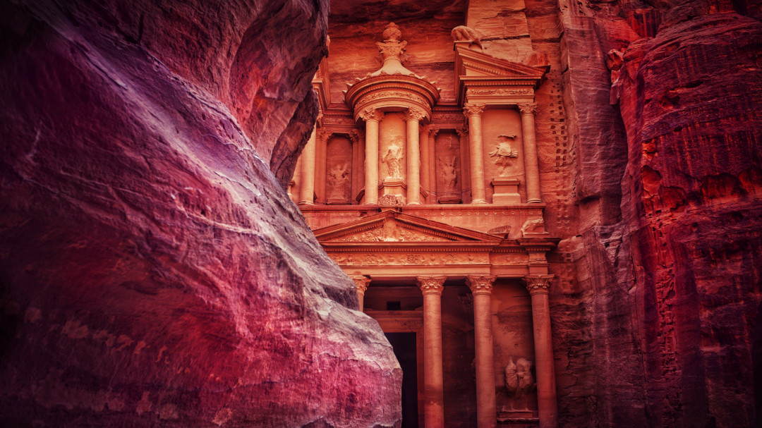 The image captures the awe-inspiring sight of Petra as seen from the Siq, a narrow and winding gorge that leads to the ancient city. The towering sandstone cliffs on both sides of the Siq create a dramatic and breathtaking entrance to Petra, inviting adventurers to step into the mysterious world of the Rose City.